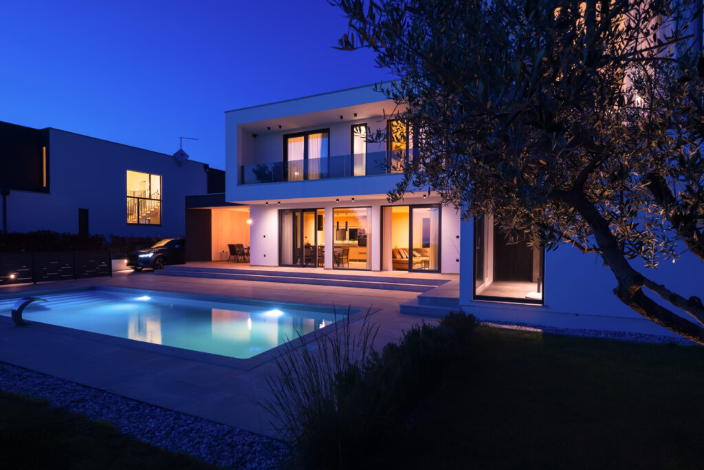 Modern luxury villa with a luminous swimming pool at twilight. Contemporary architecture, sleek design, and inviting interior lights create a serene and elegant evening ambiance, ideal for upscale living and relaxation.