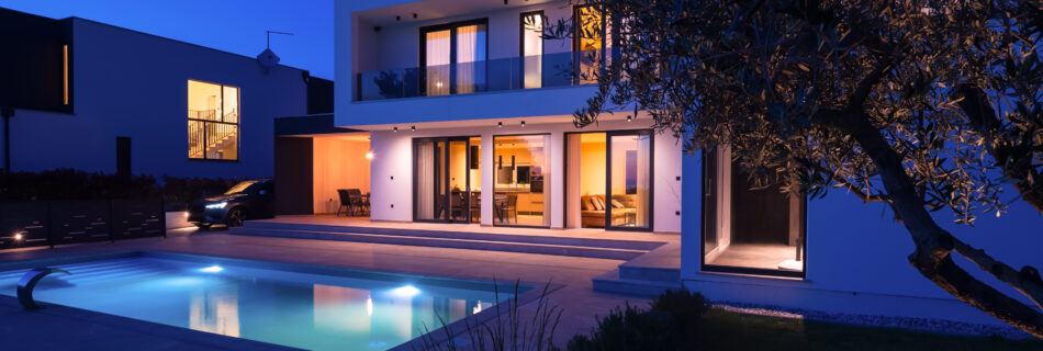 Modern luxury villa with a luminous swimming pool at twilight. Contemporary architecture, sleek design, and inviting interior lights create a serene and elegant evening ambiance, ideal for upscale living and relaxation.